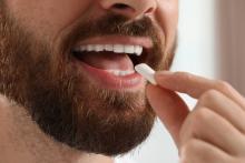 Een man met een baard doet een kauwgom in zijn mond tegen zijn slechte adem