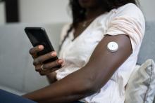 Op de arm van een vrouw met diabetes type 1 zit een suiker-sensor. Die sensor meet hoe het gaat met haar bloedsuiker. Op haar telefoon ziet ze hoe hoog of laag haar bloedsuiker is.