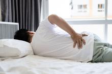 Iemand ligt op bed en grijpt naar de rug door pijn in de nieren