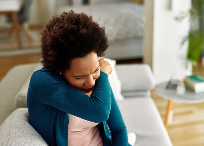 Een vrouw niest in haar elleboog door hooikoorts
