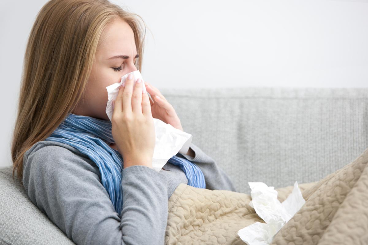 Jonge vrouw met griep hangt op de bank en snuit haar neus