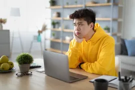 Jongere aan bureau leunt met zijn hoofd op zijn hand en kijkt vermoeid