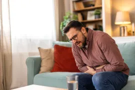 Een man zit op de bank voorovergebogen doordat hij pijn heeft van zijn prostaat-ontsteking