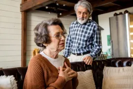 Een oudere mevrouw heeft last van haar hart. Een man kijkt bezorgd toe.